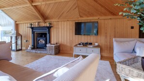 Een gezellige kamer met houten wanden en plafond, een open haard, een televisie en comfortabele zithoek.