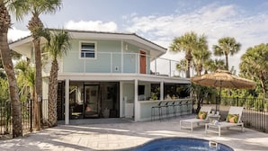 Uma casa de dois andares com piscina, área de estar ao ar livre e palmeiras.