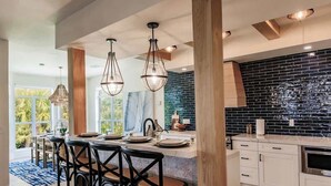 A modern kitchen with a black tiled backsplash, wooden beams, and a central island with bar stools. - Lookout Escape: Heated Pool, Golf Cart, Outdoor Bar, Gulf View (North Captiva)