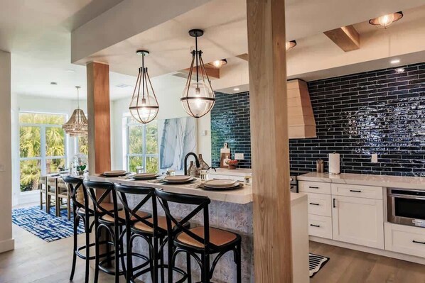 A modern kitchen with a black tiled backsplash, wooden beams, and a central island with bar stools. - Lookout Escape: Heated Pool, Free Golf Cart, Outdoor Bar, Gulf Views (North Captiva)