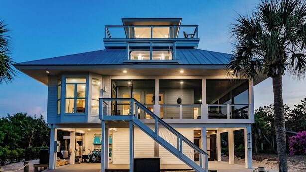 A two-story beachfront house with a balcony, a staircase leading to the upper level, and a covered outdoor area. - Lookout Escape: Heated Pool, Golf Cart, Outdoor Bar, Gulf View (North Captiva)