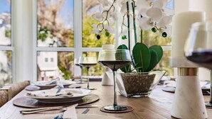 A dining table set with plates, cutlery, and a wine glass, with a view of trees through a window. - Lookout Escape: Heated Pool, Golf Cart, Outdoor Bar, Gulf View (North Captiva)