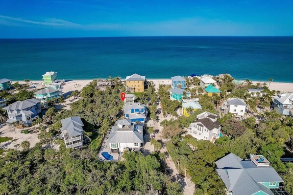 Vue aérienne d’une zone résidentielle côtière, avec des maisons, une plage et un ciel bleu dégagé.