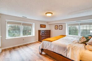 A bedroom with a large bed, two windows, a dresser, and a ceiling light.