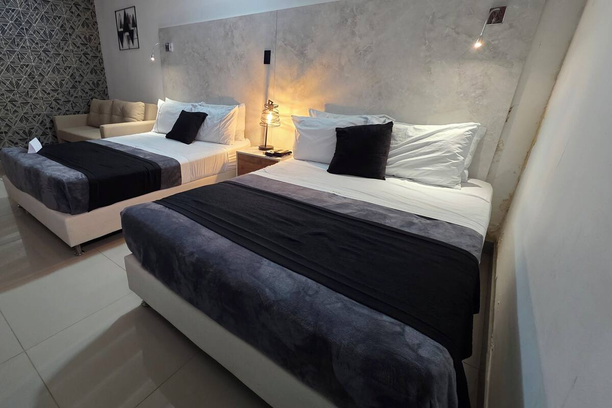 A hotel room with two beds, a sofa, a patterned wall, and a modern light fixture.