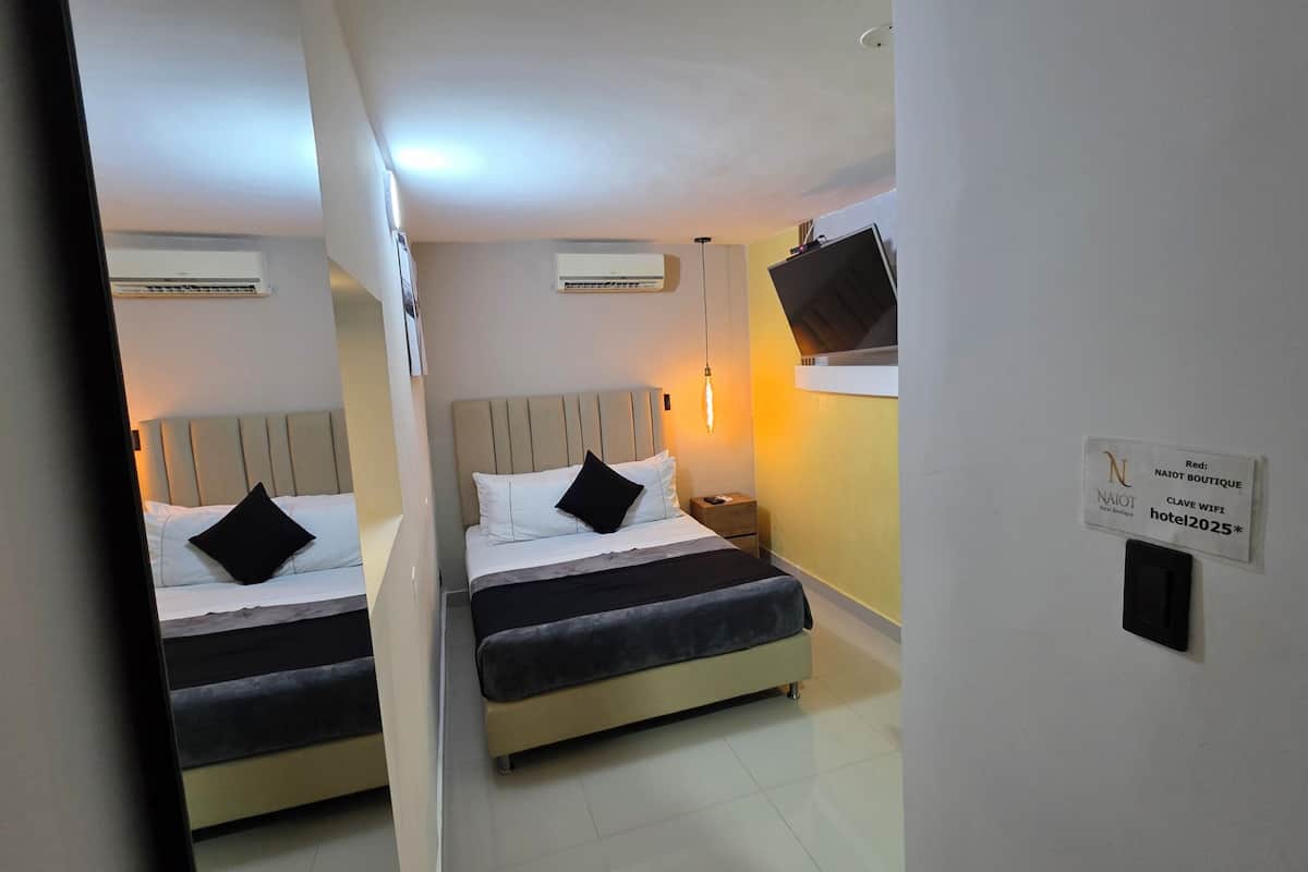 A hotel room with two beds, a nightstand, an air conditioning unit, and a wall-mounted TV.