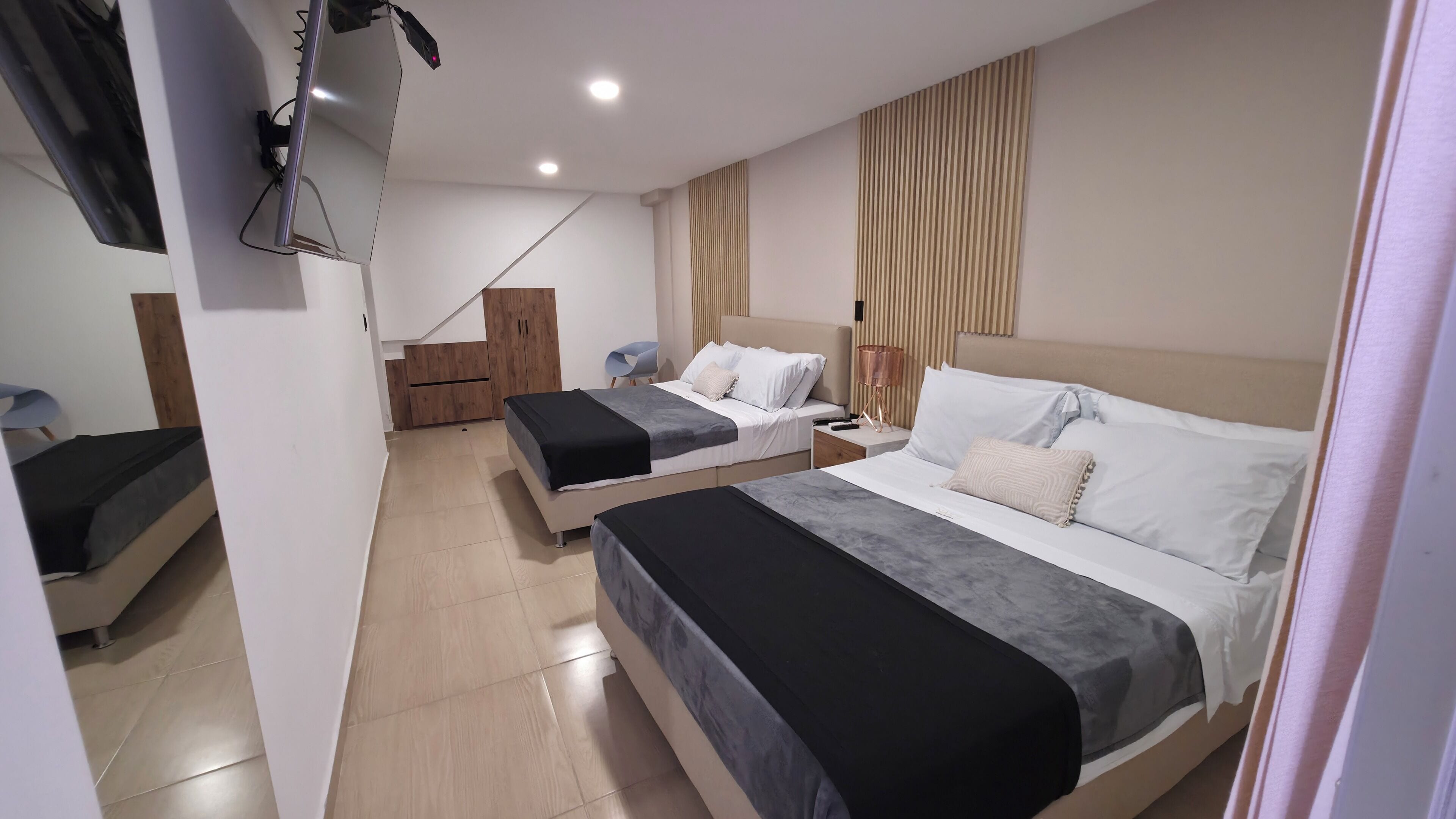 Quarto de hotel com duas camas, um guarda-roupa de madeira, uma escrivaninha e uma cadeira.