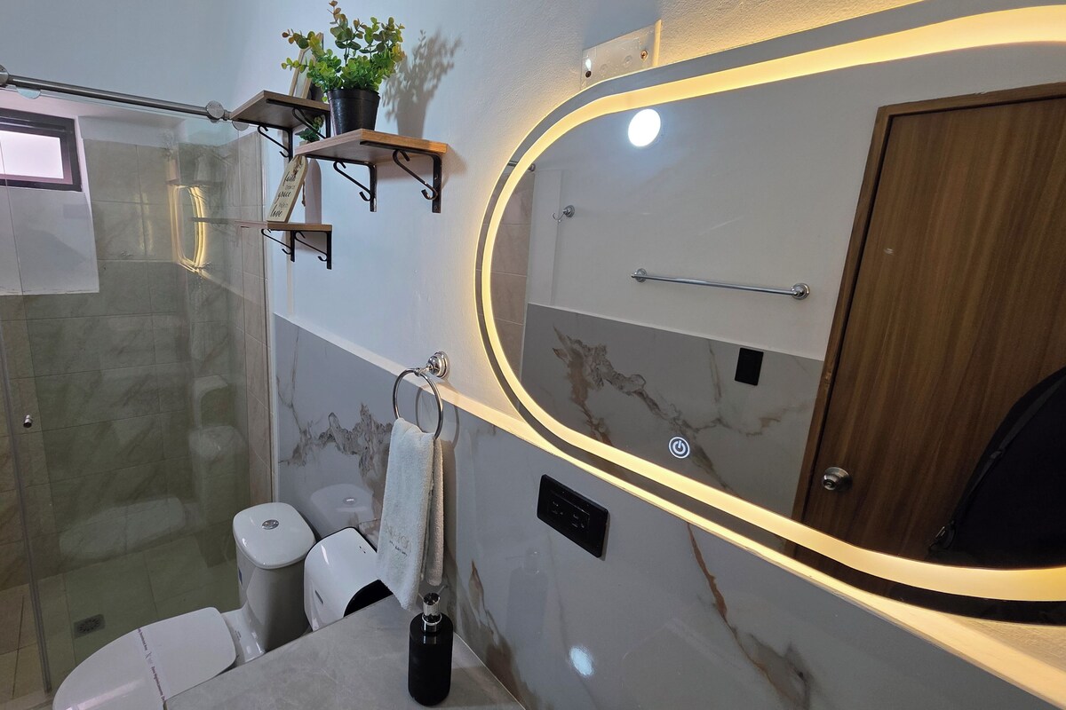 A modern bathroom with a glass shower enclosure, a marble vanity, a toilet, and a wooden door.