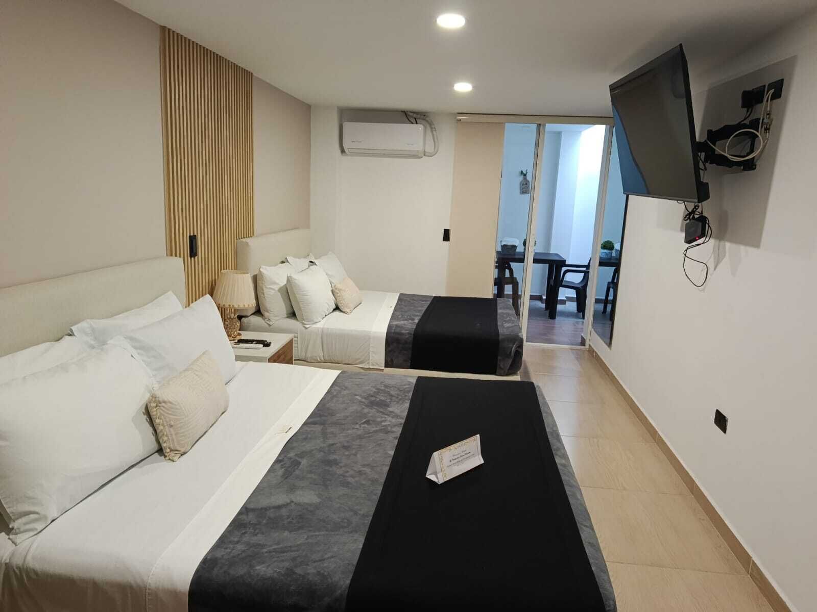 Quarto de hotel com duas camas, uma televisão fixada na parede e uma porta de correr para uma varanda.