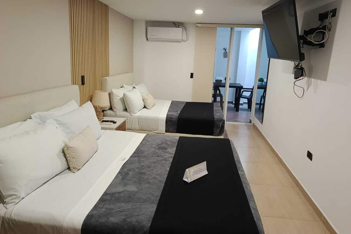 A hotel room with two beds, a TV mounted on the wall, and a sliding door leading to a balcony.