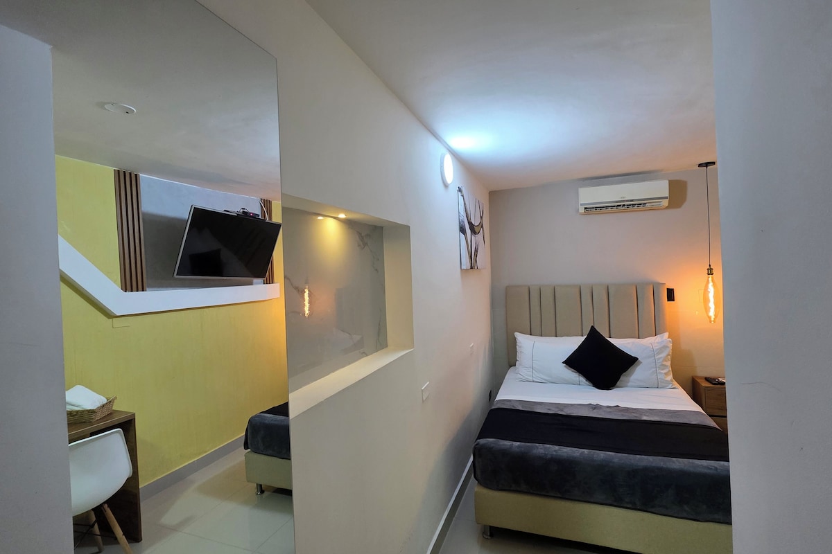 Habitació d'hotel amb llit, taula de nit i televisió penjada a la paret.