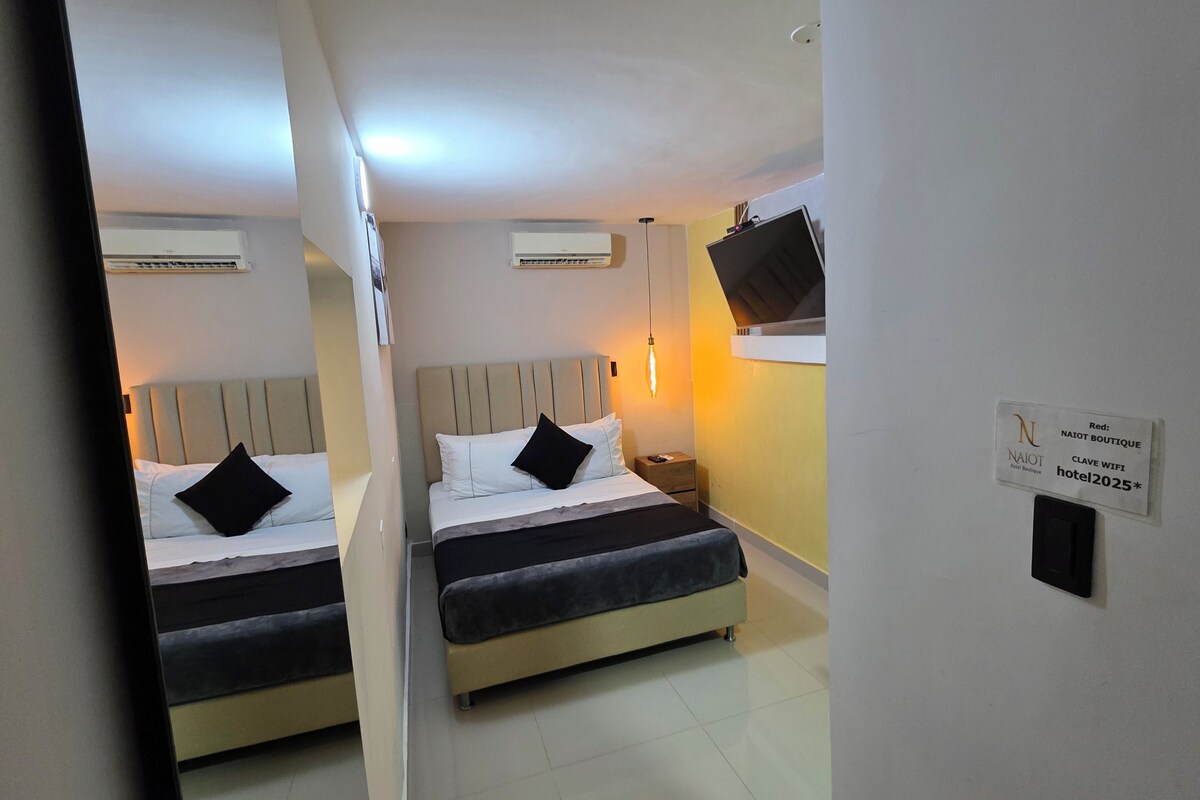 A hotel room with two beds, a nightstand, an air conditioning unit, and a wall-mounted TV.