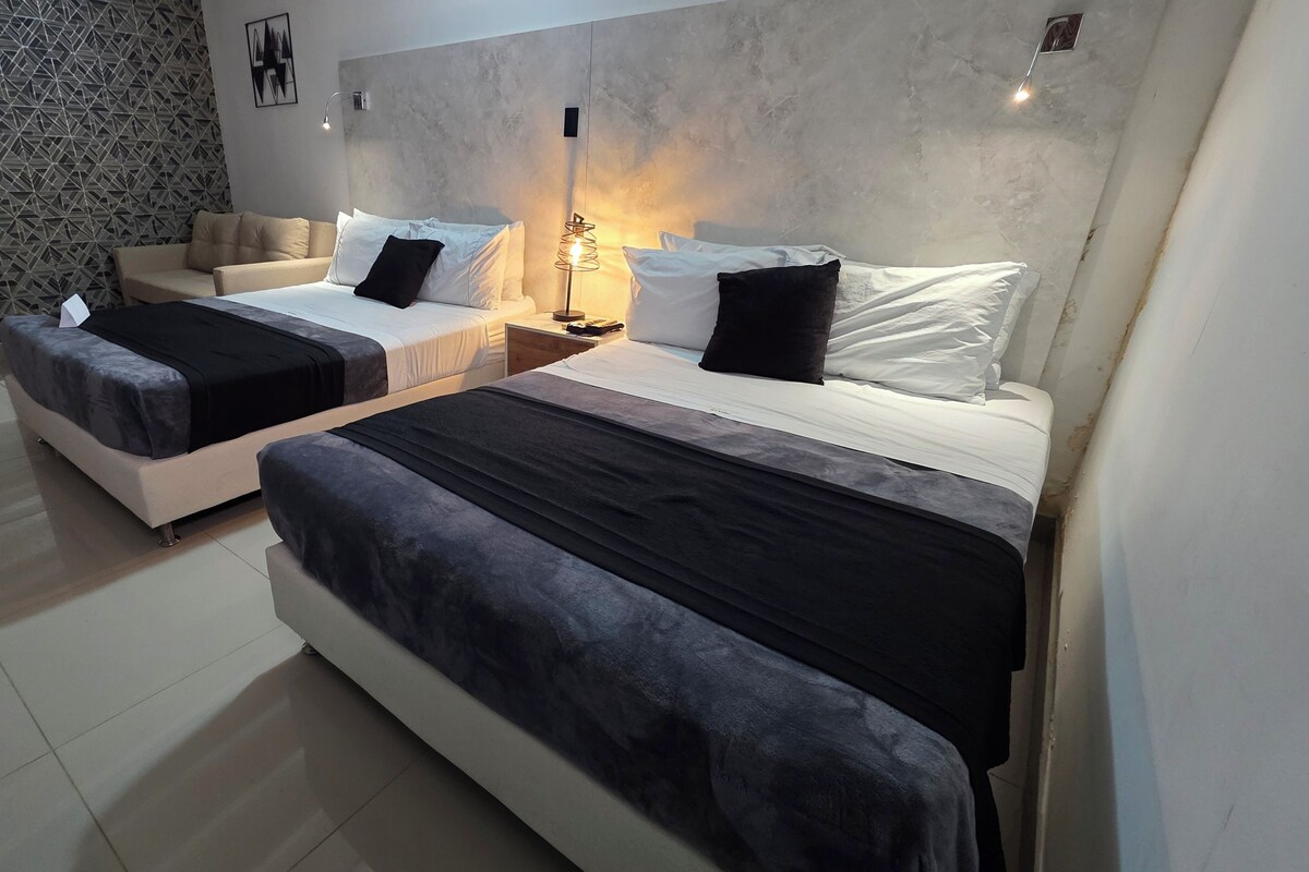 A hotel room with two beds, a sofa, a patterned wall, and a modern light fixture.