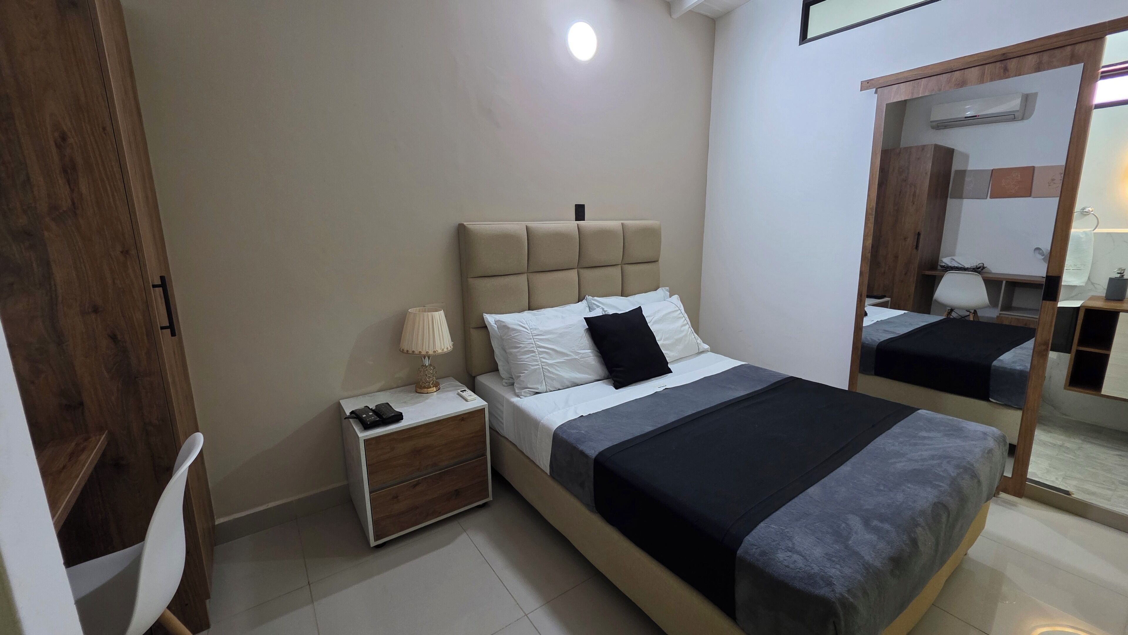 Quarto com cama, mesa de cabeceira, abajur e espelho.