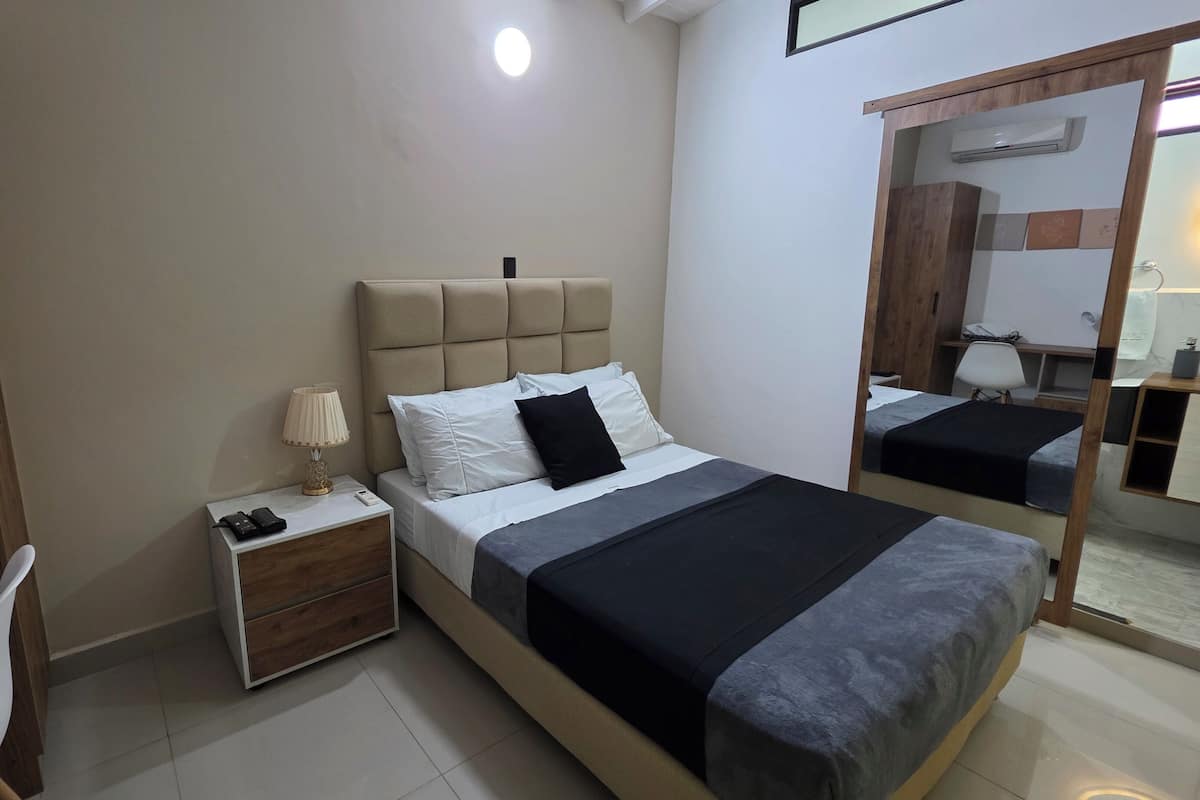 A bedroom with a bed, bedside table, lamp, and a mirror.