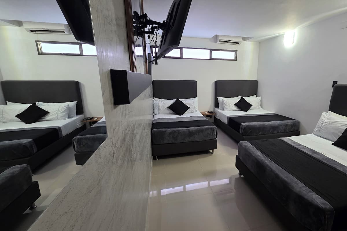 A hotel room with four beds arranged in a U-shape, a flat-screen TV mounted on the wall, and a ceiling fan.