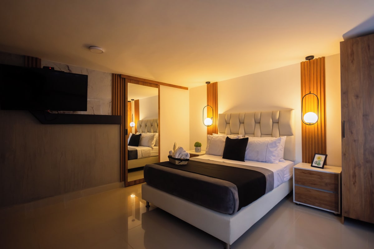 Habitació d'hotel moderna amb un llit gran, taules de nit, televisió de pantalla plana i un mirall.