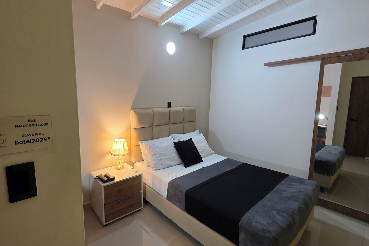 Habitació d'hotel amb llit, làmpada de nit, taulella i un cartell que indica el nom de l'hotel i els serveis.
