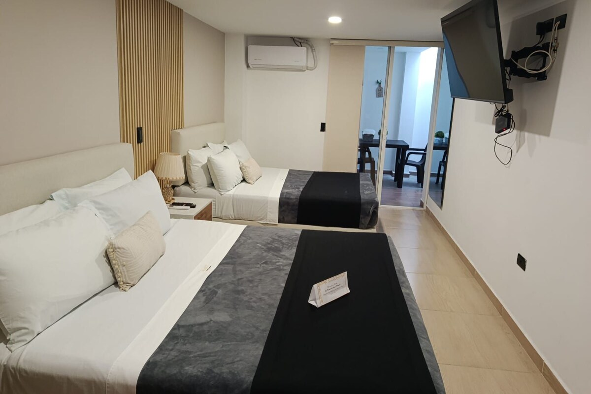 Habitació d'hotel amb dos llits, un televisor penjat a la paret i una porta corredissa que dona a un balcó.