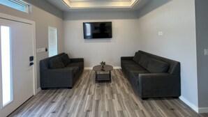 Un salon moderne avec deux canapés, une table basse, un ventilateur de plafond et un téléviseur à écran plat fixé au mur.
