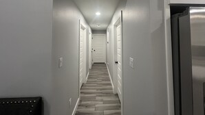 Un couloir étroit avec un plancher en bois, des murs blancs et une porte au fond.