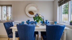 Un comedor con una mesa blanca, sillas tapizadas en azul y un espejo redondo en la pared.