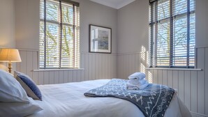 Una cama bien hecha con un edredón estampado, una lámpara y un cuadro en la pared.
