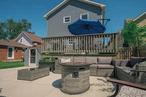 Un patio trasero con un brasero, mobiliario exterior y una terraza de madera.