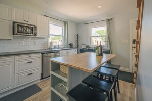 Una cocina con armarios blancos, un microondas, un fregadero y una isla de madera con taburetes.