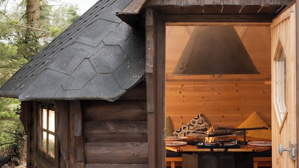 A rustic cabin with a chimney, a dining table, and a fireplace inside.