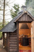 A rustic cabin with a chimney, a dining table, and a fireplace inside.
