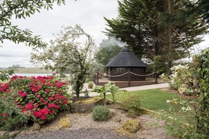A rustic cabin with a thatched roof, surrounded by lush greenery and flowering plants.