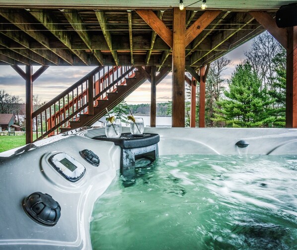Un jacuzzi debajo de una terraza de madera con una escalera que lleva a una casa.