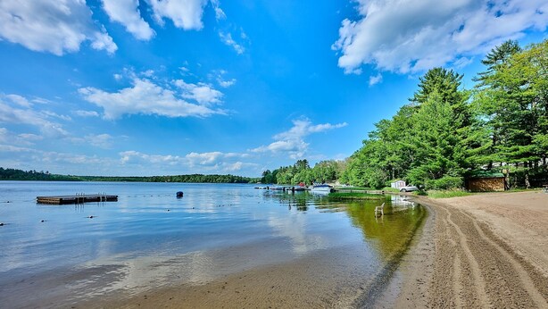 Eine Uferlandschaft mit Sandstrand, ruhigem Wasser und einer Anlegestelle.