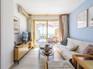 A living room with a sofa, TV, wooden side table, and a balcony with outdoor furniture.