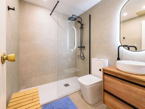 A modern bathroom with a glass-enclosed shower, a white toilet, and a wooden vanity with a sink. - Cosy apartment for 6 people with A/C, WIFI, TV and terrace (Salou)