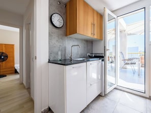 A modern kitchen with a clock, wooden cabinets, a sink, and a sliding glass door leading to an outdoor area. - Cosy apartment for 6 people with A/C, WIFI, TV and terrace (Salou)