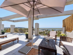 An outdoor patio with a table, chairs, an umbrella, and a view of the sea.