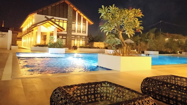 A modern hotel with a swimming pool, outdoor seating, and well-lit surroundings.