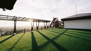 A rooftop terrace with a pergola, a white building, and a view of the horizon.