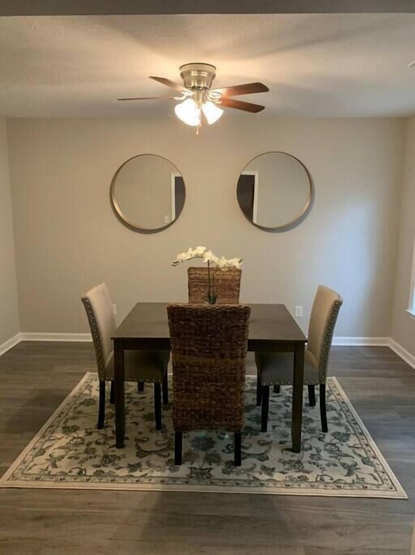 A dining room with a table, chairs, a rug, and two wall-mounted mirrors.