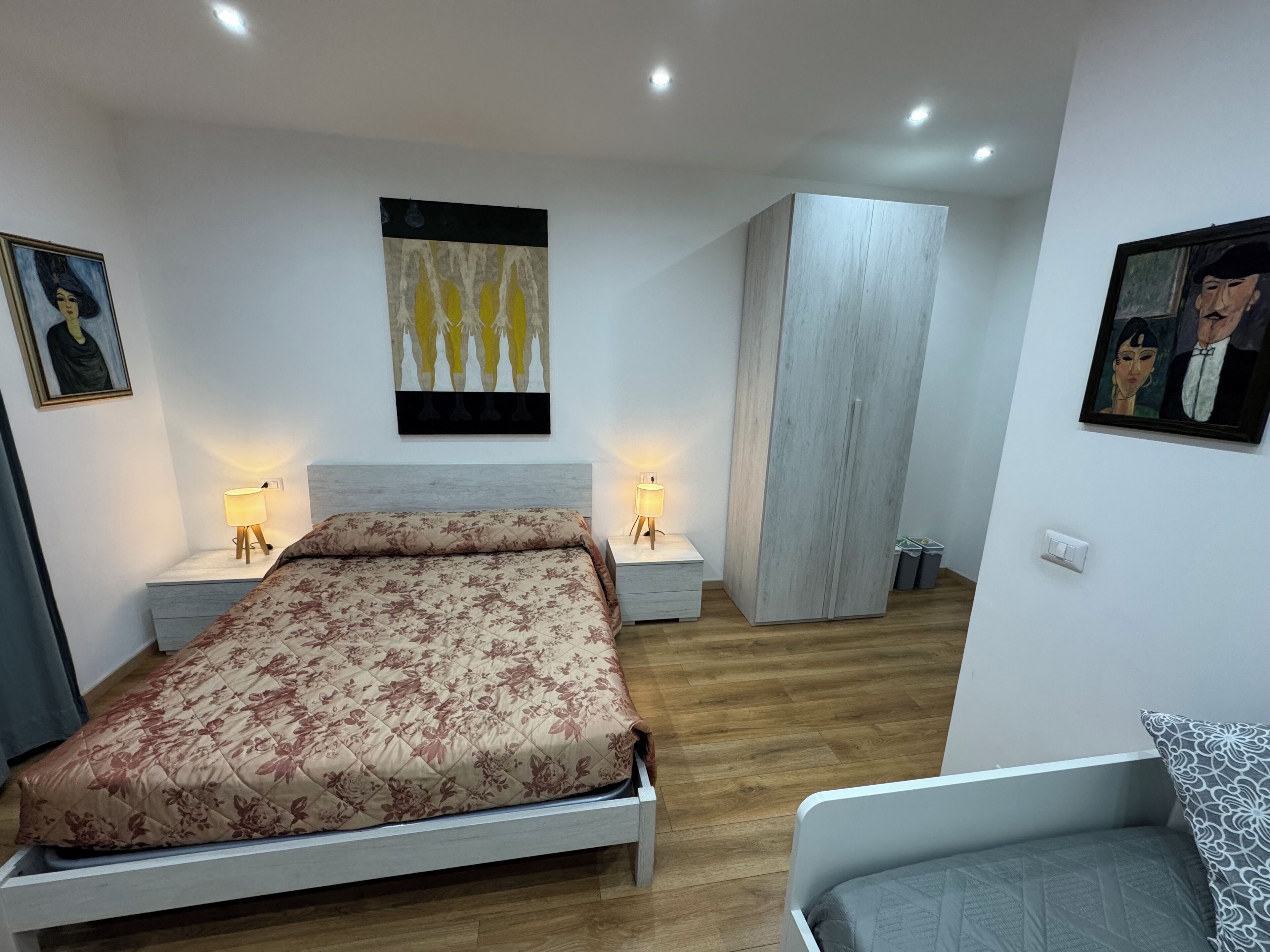 Una camera da letto moderna con un letto, due comodini con lampade, un armadio e opere d'arte alle pareti.