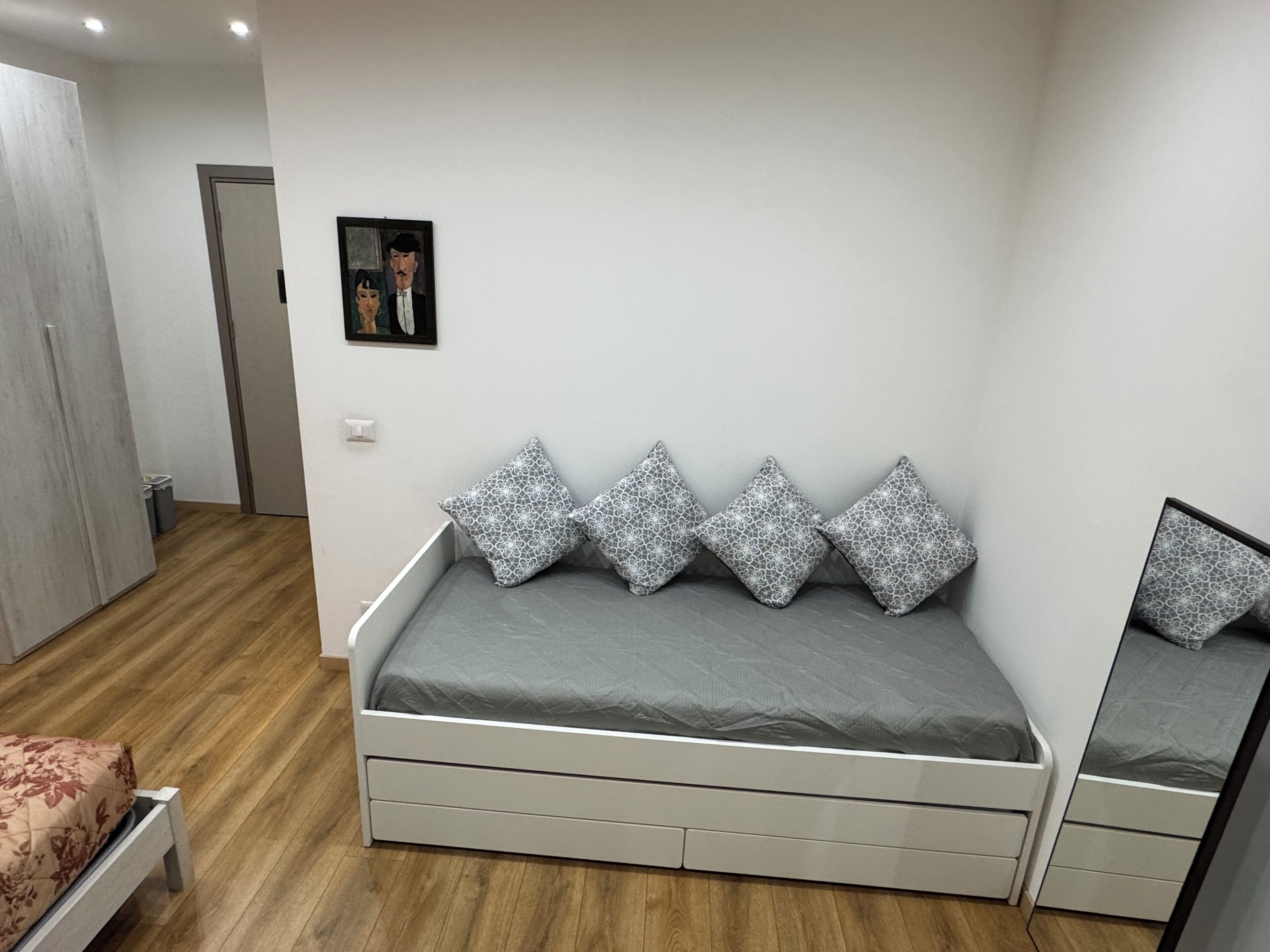 Un dormitorio con cama, mesita de noche, espejo, armario y un cuadro en la pared.