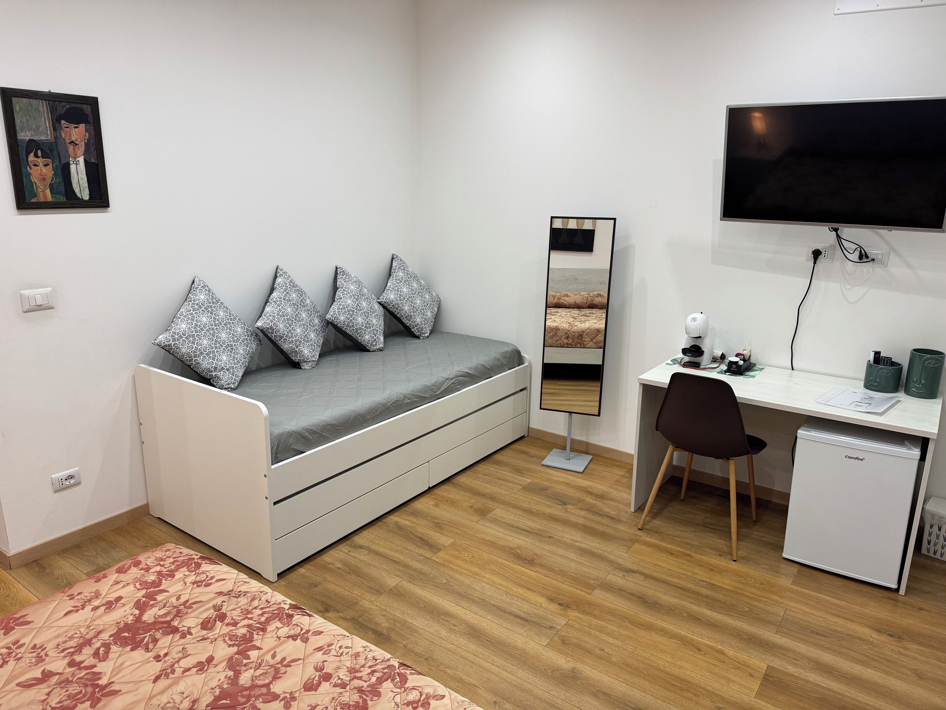 Ein kleines Zimmer mit Bett, Schreibtisch, Stuhl, Fernseher und kleinem Kühlschrank.