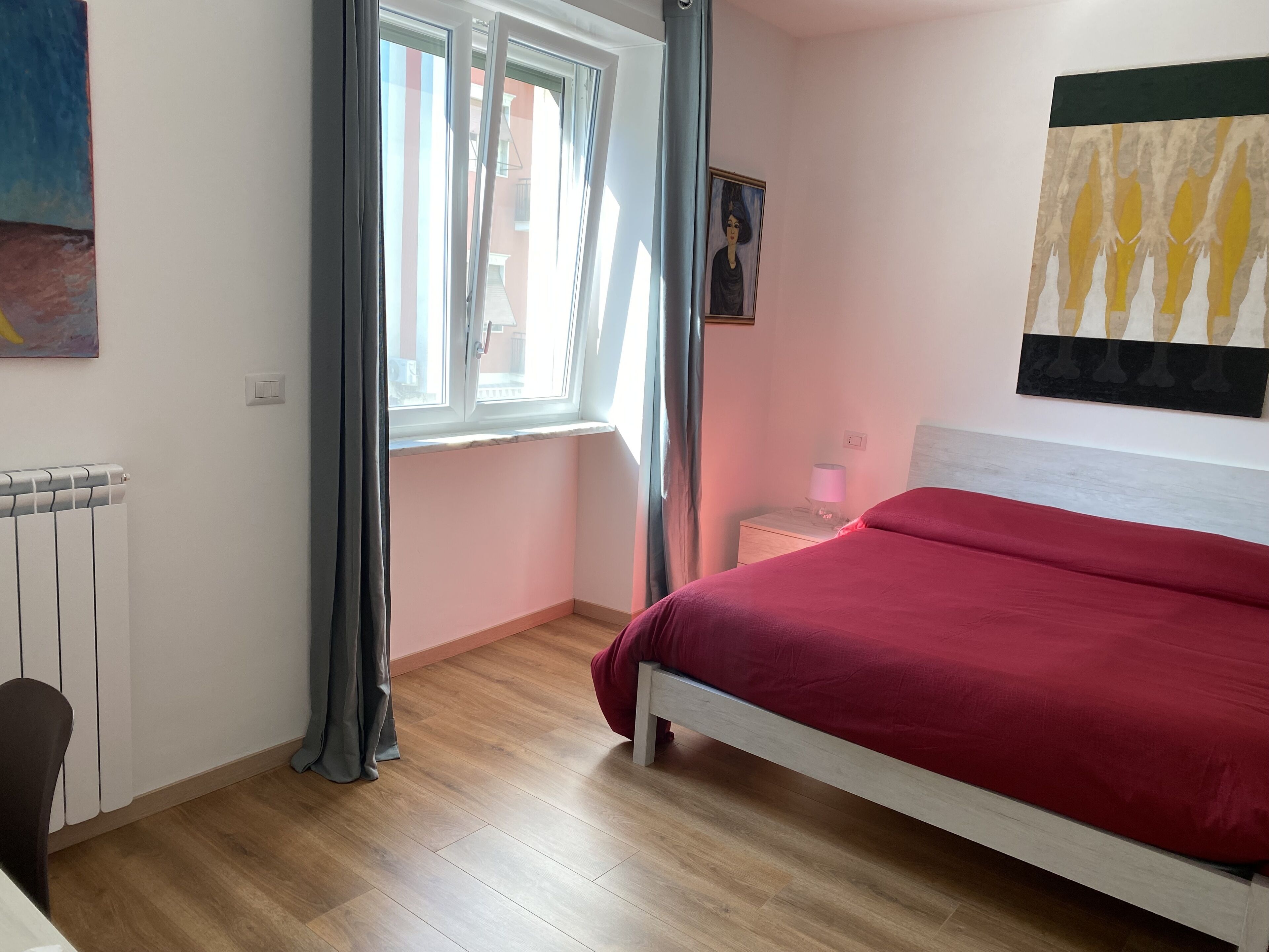 Un dormitorio con una cama, una ventana con cortinas, un radiador y un cuadro en la pared.