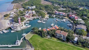Vista aérea de un puerto deportivo con barcos amarrados, un faro y edificios circundantes.