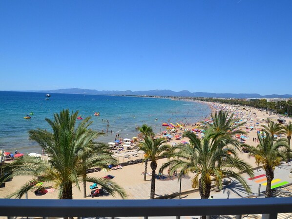 A beach with palm trees, umbrellas, and people.