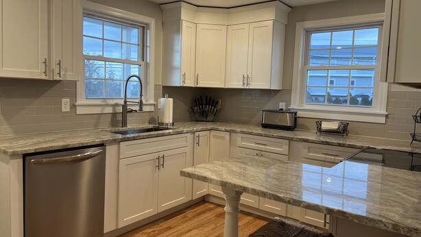 A modern kitchen with white cabinets, a stainless steel dishwasher, and a marble countertop. - Unwind Oceanside
Private single family home (Hampton)