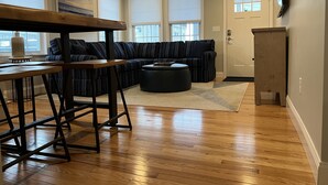 A modern living room with a wooden dining table, striped sofa, and a black ottoman. - Unwind Oceanside
Private single family home (Hampton)