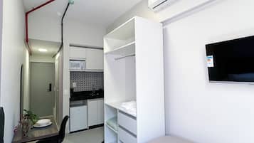 Ein kompaktes Hotelzimmer mit Bett, Schreibtisch mit Stuhl, Küchenzeile, Kleiderschrank und einem Wand-Fernseher.